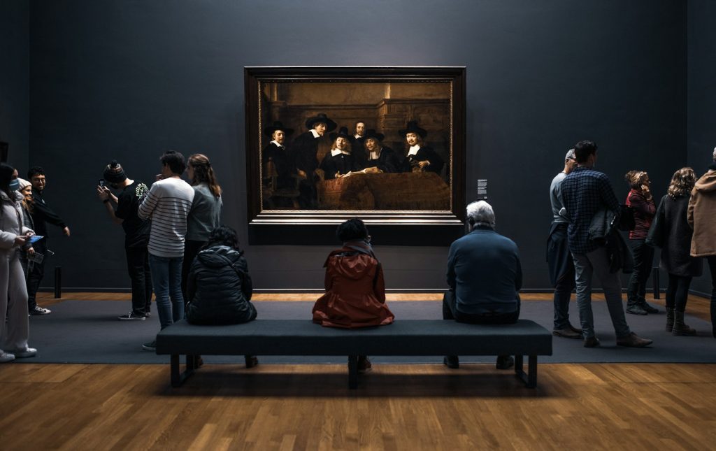 a group of people standing around a museum looking at a painting